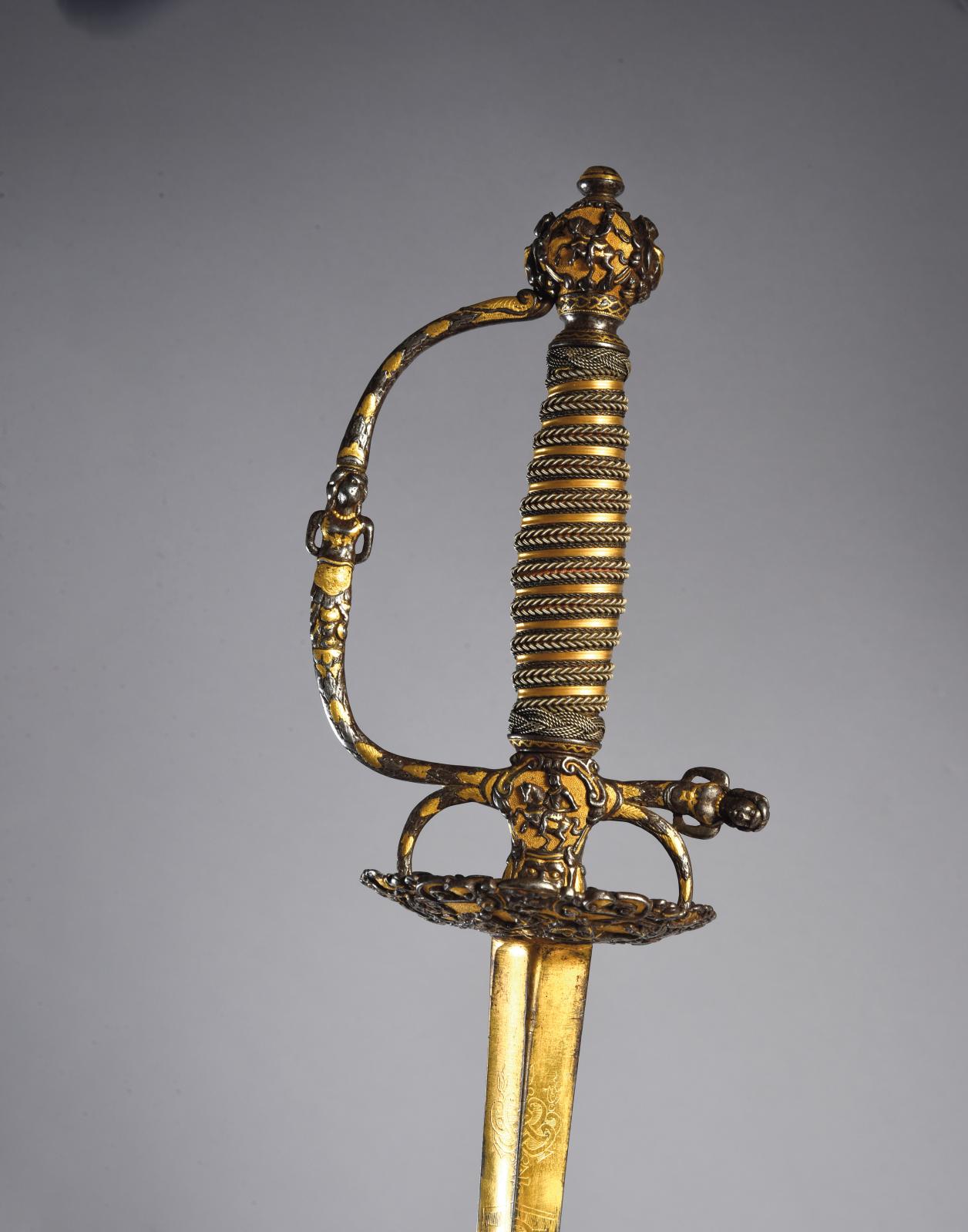 Épée de cour ayant appartenu au baron de Breteuil, garde à une branche en fer ciselé en relief de cavaliers et guirlandes sur fond d’or am