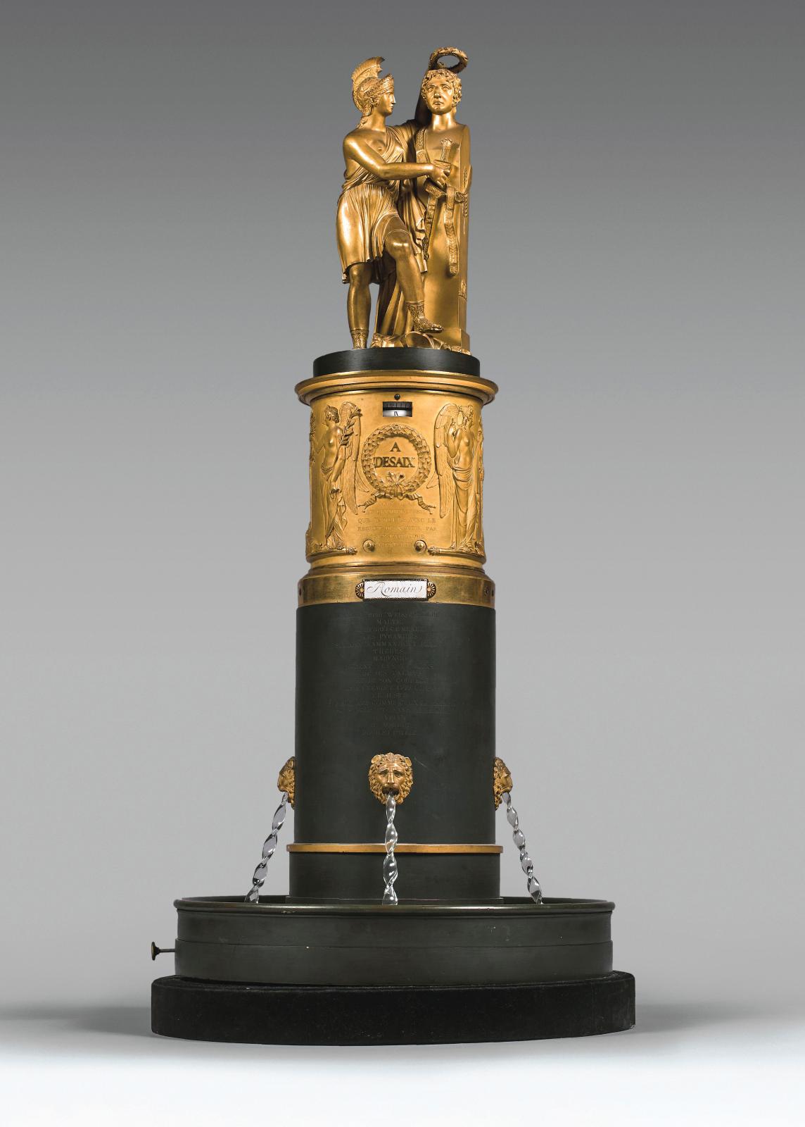 Époque Empire. Pendule simulant une fontaine en bronze doré et bronze patiné surmontée d’une statue allégorique à la mémoire du général De