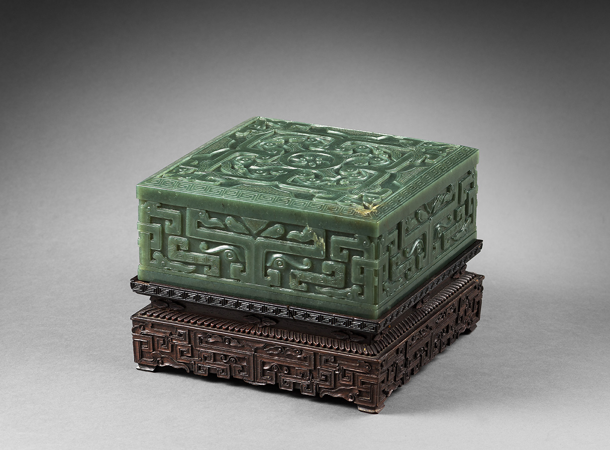 Chine, début XXe siècle. Boîte de forme carrée en néphrite verte à décor sculpté sur le couvercle d’un carré formé par quatre masques de t